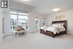 Spacious sleeping area featuring expansive window treatments, neutral wall tones, recessed ceiling details, light-toned carpet flooring, and a glass-paneled door - 