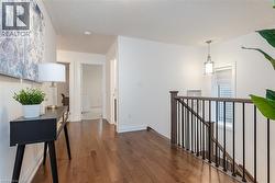 Hardwood flooring extends throughout the hallway, featuring a wood-finish staircase railing with black metal balusters - 