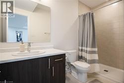 Contemporary bathroom featuring a dark wood-finish vanity with a white countertop and oval sink, a wall-mounted mirrored medicine cabinet, a toilet, and a shower with light-toned tiled walls - 