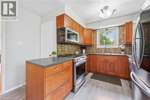 Kitchen featuring wood-finish cabinetry, stainless steel appliances, dark countertops, a mosaic tile backsplash, and light wood-finish flooring - 24 Byton Lane, Cambridge, ON 