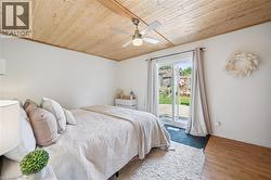 Room featuring a wood-panel ceiling with a ceiling fan, white walls, and a sliding glass door providing access to a deck and fenced backyard - 