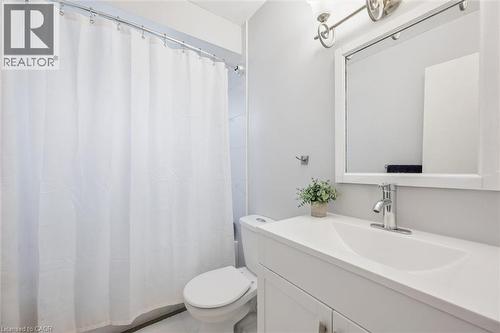 Bathroom featuring a white vanity with integrated sink, chrome faucet, wall-mounted mirror, and a toilet - 24 Byton Lane, Cambridge, ON 