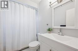 Bathroom featuring a white vanity with integrated sink, chrome faucet, wall-mounted mirror, and a toilet - 