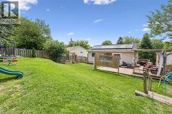 Expansive backyard featuring a large wooden deck with a pergola, a sloped grassy lawn, a privacy fence, and raised garden beds - 