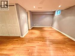 Spacious room featuring wood-finish flooring, light grey walls, white baseboards, a white bi-fold closet, and recessed lighting - 