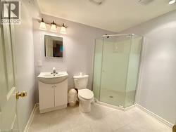 Bathroom featuring a corner shower enclosure with clear glass panels, a single-sink vanity with cabinet storage, a wall-mounted mirror, and a three-light vanity fixture - 