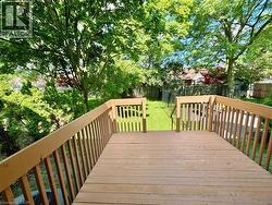Spacious outdoor deck with wood-finish flooring and sturdy railings overlooking a fenced backyard with mature trees and a manicured lawn - 