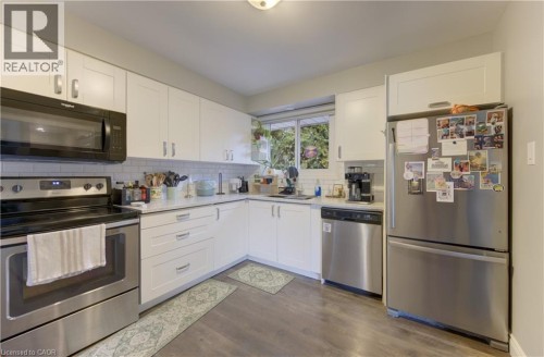 Kitchen featuring white shaker-style cabinetry, wood-finish flooring, stainless steel appliances, and a subway tile backsplash - 127 Strathcona Crescent, Kitchener, ON 