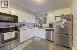 Kitchen featuring white shaker-style cabinetry, wood-finish flooring, stainless steel appliances, and a subway tile backsplash - 