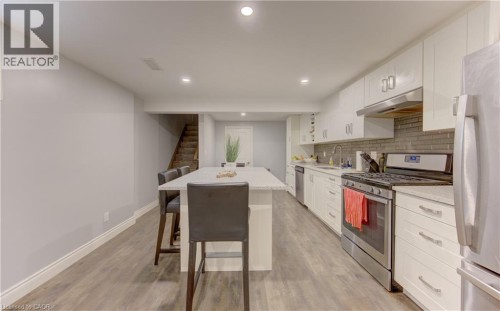 Spacious kitchen featuring white cabinetry, stainless steel appliances, a tile backsplash, and wood-finish flooring - 127 Strathcona Crescent, Kitchener, ON 