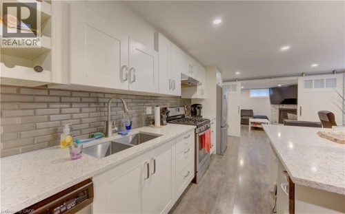 Modern kitchen featuring white shaker cabinetry, stainless steel appliances, a double basin sink, and a light-toned brick-patterned tile backsplash - 127 Strathcona Crescent, Kitchener, ON 
