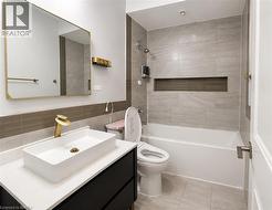 Bathroom featuring a rectangular vessel sink with a gold-tone faucet, a dark vanity cabinet, a wall-mounted mirror with a gold-tone frame, a bathtub with a tiled surround, and a recessed shower niche - 