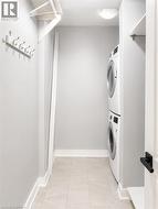 Utility space featuring a stacked washer and dryer unit, light gray tile flooring, shelving, a coat rack, and recessed lighting - 