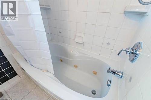 Soaking tub with integrated jets, chrome fixtures, and white tiled surround with decorative accents - 1293 Daimler Road, Mississauga, ON 