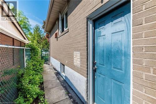 Brick exterior with an entryway door, a concrete pathway, a chain-link fence, and established greenery - 1293 Daimler Road, Mississauga, ON 