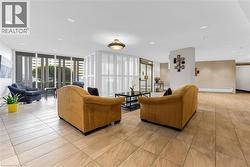 Lobby area featuring large format floor tiling, a bank of full-height windows, a prominent wall of white shutters, a central column, and recessed lighting - 