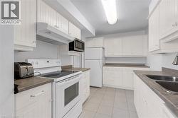 Kitchen featuring white cabinetry, integrated appliances, a double basin stainless steel sink, and light tile flooring - 
