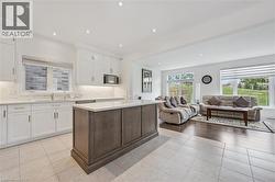 Open-concept kitchen and living area featuring white cabinetry, a central island with a lighter countertop, recessed lighting, and tile flooring - 