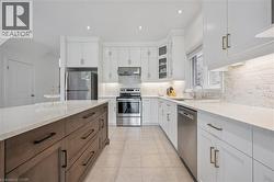 Contemporary kitchen featuring a two-toned island with ample storage, white cabinetry, integrated stainless steel appliances, a tile backsplash, and recessed lighting - 