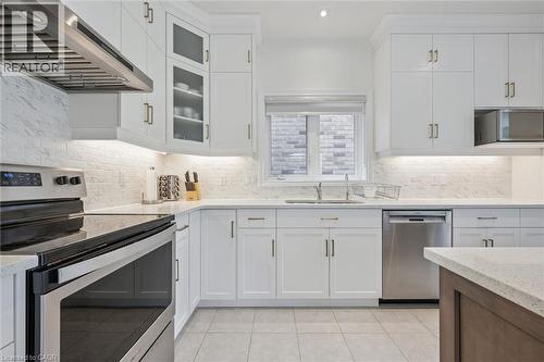 Bright kitchen featuring white shaker cabinetry with brushed gold hardware, stainless steel appliances, light-toned tile flooring, and a subway tile backsplash - 153 Rivertrail Avenue, Kitchener, ON - Indoor Photo Showing Kitchen With Upgraded Kitchen