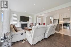 Open-concept living space featuring wood-finish flooring, a contemporary fireplace with mantel, recessed lighting, and a kitchen with white cabinetry, a wood-finish island, and stainless steel applian - 