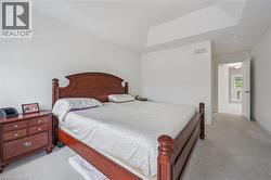 Carpeted bedroom featuring a tray ceiling, white walls, and a doorway leading to another area - 