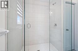 Glass-enclosed shower featuring white wall tiling, a tiled floor, and chrome fixtures - 
