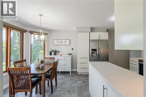 Kitchen and dining area featuring a breakfast bar with a light-toned countertop, stainless steel refrigerator, white cabinetry, and gray tile flooring - 141 Lynndale Road, Simcoe, ON 