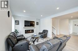 Living area with light wood-style floors, a glass covered fireplace, recessed lighting, and stairway - 
