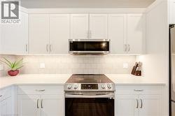 Kitchen with stainless steel appliances, white cabinetry, tasteful backsplash, and light stone counters - 