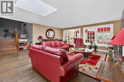 Spacious living area featuring wood-finish flooring, a skylight, and large windows with white louvered shutters - 