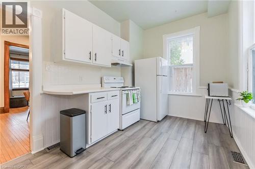 Kitchen featuring wood-finish plank flooring, white cabinetry with dark hardware, white appliances, and a white subway tile backsplash - 67 Ahrens Street W, Kitchener, ON 