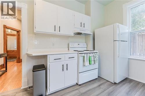 Kitchen featuring white cabinetry with dark hardware, white countertops, and a white tile backsplash - 67 Ahrens Street W, Kitchener, ON 