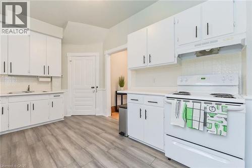 Kitchen featuring wood-finish flooring, white cabinetry with dark hardware, a white electric range, and a white tile backsplash - 67 Ahrens Street W, Kitchener, ON 