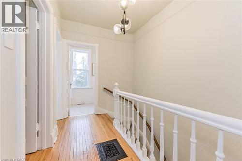 Hallway featuring wood-finish flooring, a contemporary ceiling light fixture, a window with architectural trim, a white painted railing, and light-toned walls - 67 Ahrens Street W, Kitchener, ON 