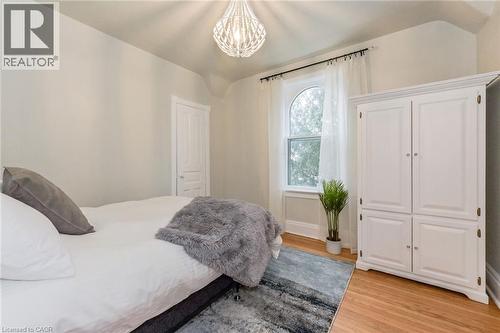 Bedroom featuring a vaulted ceiling with an ornate chandelier, a large arched window with sheer drapes, wood-finish flooring, and a paneled wardrobe - 67 Ahrens Street W, Kitchener, ON 