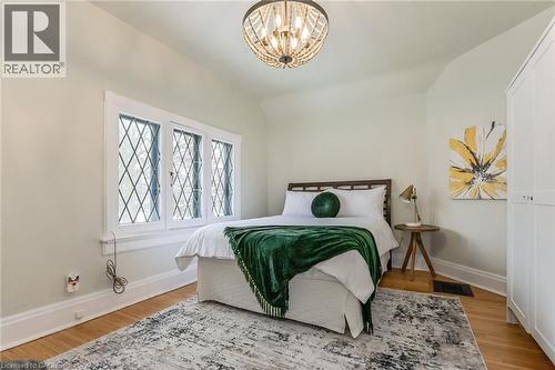 Bedroom featuring diamond-pane windows, wood-finish flooring, a contemporary ceiling light fixture, and a built-in white wardrobe - 67 Ahrens Street W, Kitchener, ON 