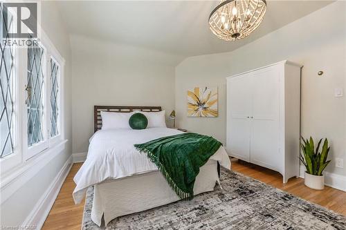 Bedroom featuring diamond-pane windows, wood-finish flooring, a built-in wardrobe, and a decorative ceiling light fixture - 67 Ahrens Street W, Kitchener, ON 