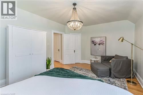 Bedroom featuring hardwood-style flooring, a decorative beaded chandelier, white trim, and light-toned walls - 67 Ahrens Street W, Kitchener, ON 