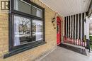 Brick exterior featuring a red arched entry door, black-framed windows, a striped privacy screen, and a covered porch with a white plank ceiling - 67 Ahrens Street W, Kitchener, ON 