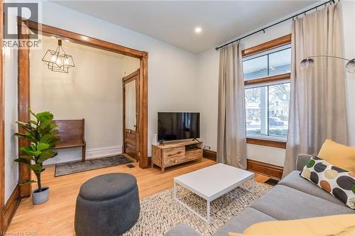 Bright living area featuring wood-finish flooring, white walls, and substantial natural light from a large window - 67 Ahrens Street W, Kitchener, ON 
