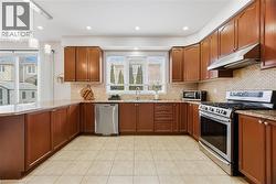 Kitchen with stainless steel appliances, light stone countertops, wood finish cabinets, a peninsula, and backsplash - 