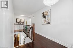 Hall with an upstairs landing, dark wood-style floors, and hanging lights - 