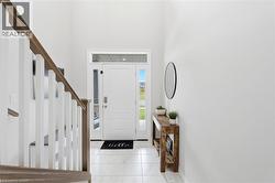 Bright foyer featuring a staircase with wood-finish handrail, white balusters, and a white entry door with sidelight and transom window - 