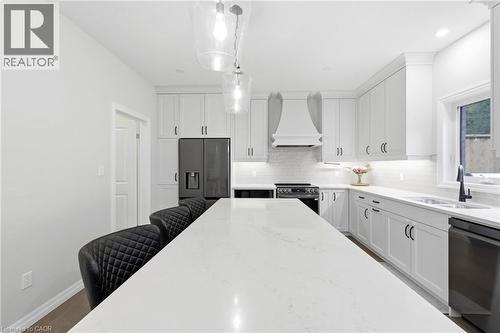 Spacious kitchen featuring an extended center island with light-toned countertop, white cabinetry with dark hardware, built-in range hood, and matte black appliances - 39 Dunning Way, St. Thomas, ON 