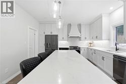 Spacious kitchen featuring an extended center island with light-toned countertop, white cabinetry with dark hardware, built-in range hood, and matte black appliances - 