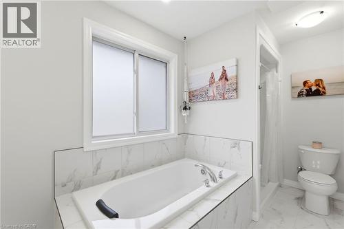 Deep-set soaking tub with deck-mounted chrome fixtures, surrounded by white marbled tile - 39 Dunning Way, St. Thomas, ON 