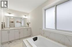 Bathroom featuring a built-in bathtub, a double vanity with light-colored countertops, dual sinks with individual faucets, and a large mirror extending across the vanity - 