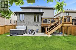 Expansive backyard featuring a manicured lawn, a concrete patio with a hot tub, and a multi-level wooden deck with privacy screening and balusters - 