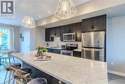 Contemporary kitchen featuring a large island with a light-toned countertop, dark cabinetry, stainless steel appliances, and geometric pendant lighting - 